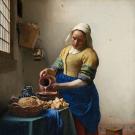 Femme vêtue portant un bonnet blanc et versant du lait dans un récipient.
