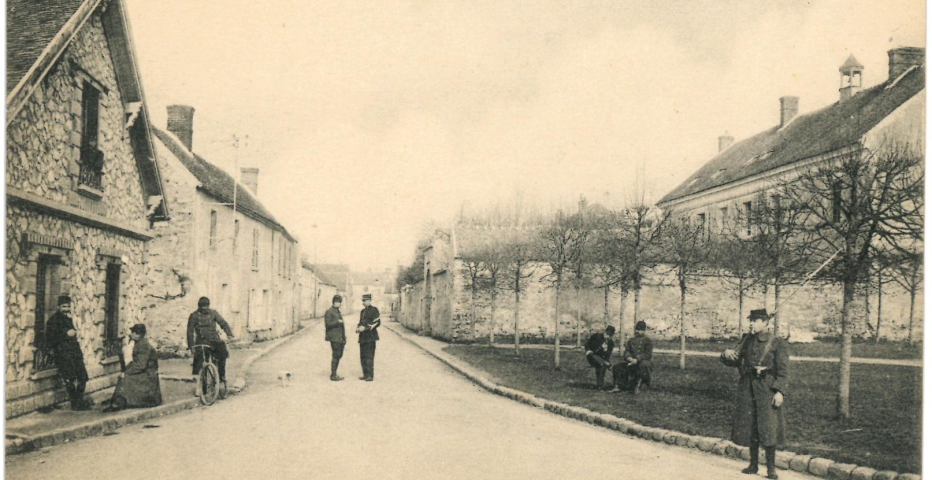Carte postale, vue d'une rue de Fleury-en-Brie, des hommes en uniformes et armés sont postés dans la rue.