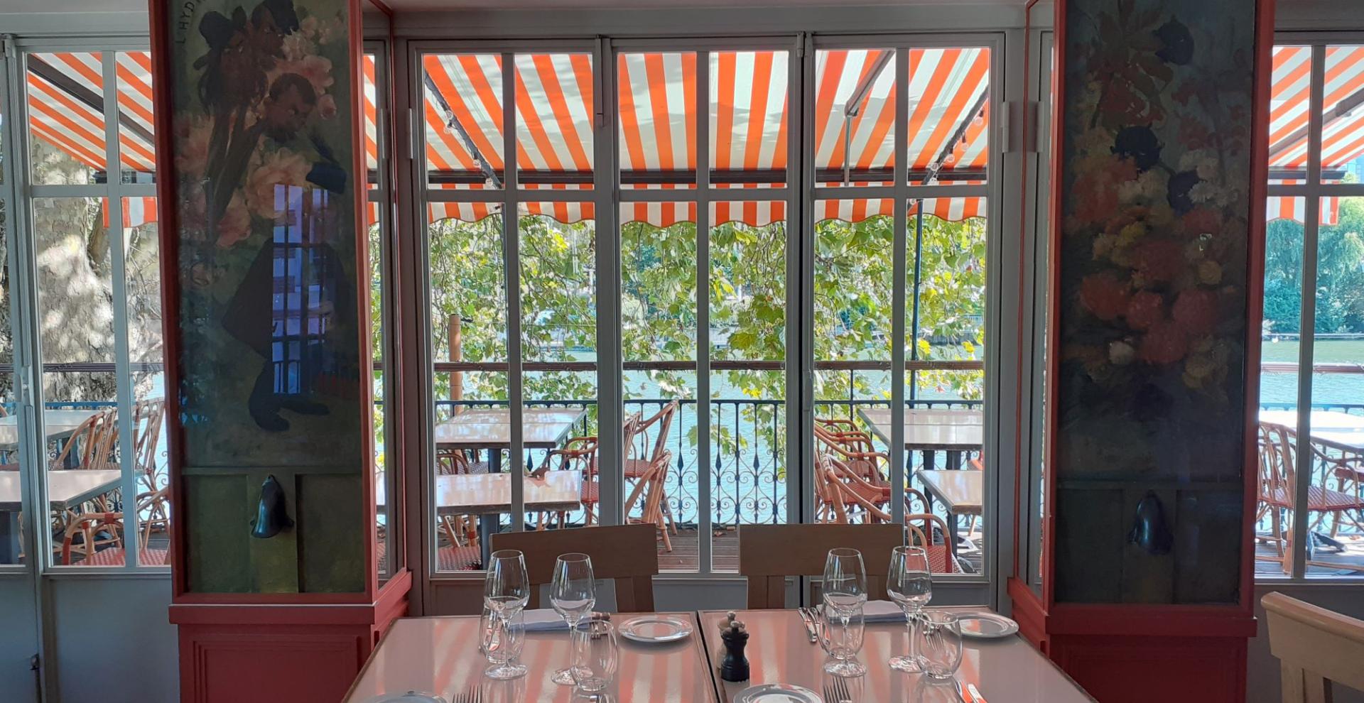 intérieur de restaurant, table dressée au premier plan, chaises et table sur une terrasse en arrière plan