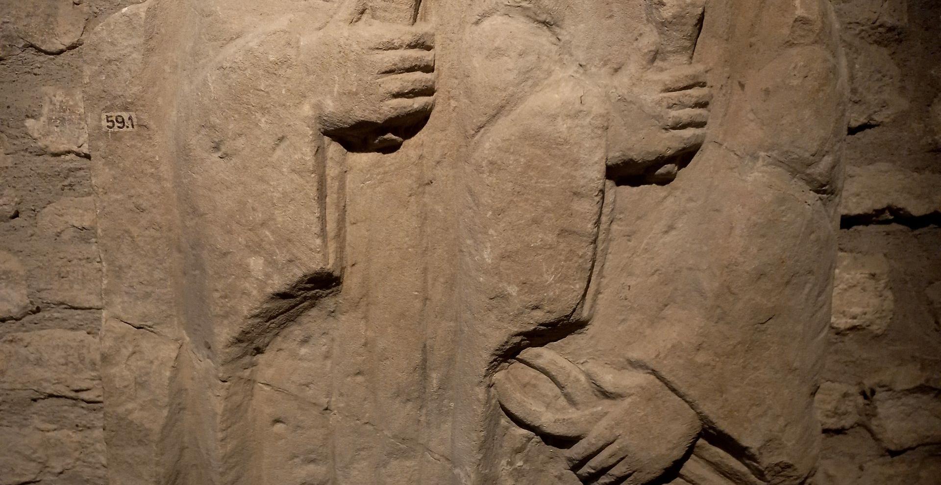 Sculture en relief de deux personnages en vêtements hamples, tenant une pince et un coin 