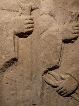 Sculture en relief de deux personnages en vêtements hamples, tenant une pince et un coin 