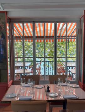 intérieur de restaurant, table dressée au premier plan, chaises et table sur une terrasse en arrière plan
