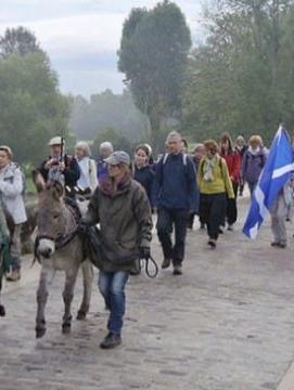 groupe de personnes marchant sur un pont de pierres, des enfants sont à dos d'ânes