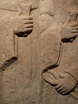 Sculture en relief de deux personnages en vêtements hamples, tenant une pince et un coin 