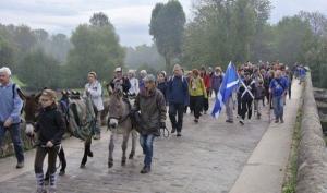 groupe de personnes marchant sur un pont de pierres, des enfants sont à dos d'ânes