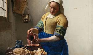 Femme vêtue portant un bonnet blanc et versant du lait dans un récipient.