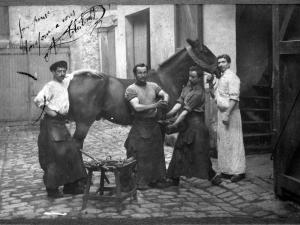 Quatre hommes posent dans des tenues de maréchaux, l'un est accoudé sur la croupe du cheval, l'un tient le cheval en longe et les deux autres tiennent le pied du cheval