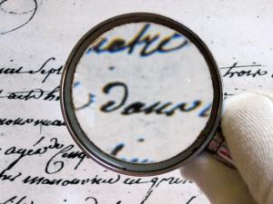 Main tenant une loupe sur un texte ancien, exercice de paléographie