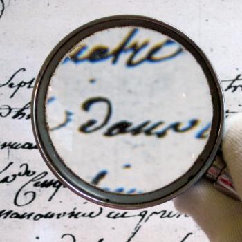 Main tenant une loupe sur un texte ancien, exercice de paléographie