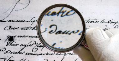 Main tenant une loupe sur un texte ancien, exercice de paléographie