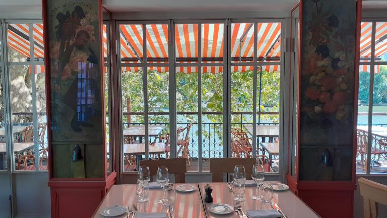 intérieur de restaurant, table dressée au premier plan, chaises et table sur une terrasse en arrière plan